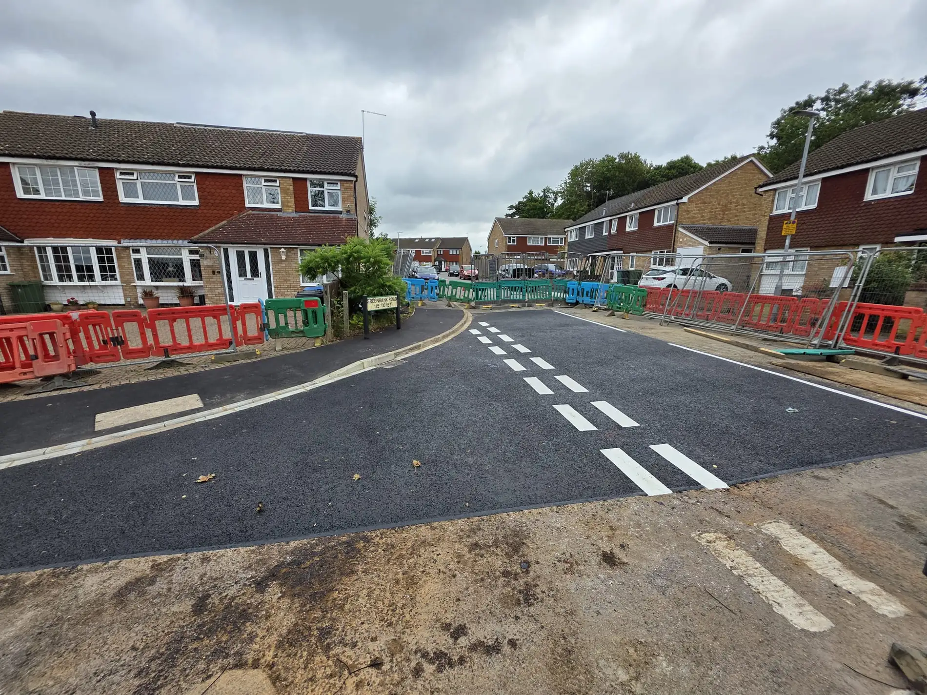Residential carriageway resurfaced and re-lined, with site barriers still in place along the kerb